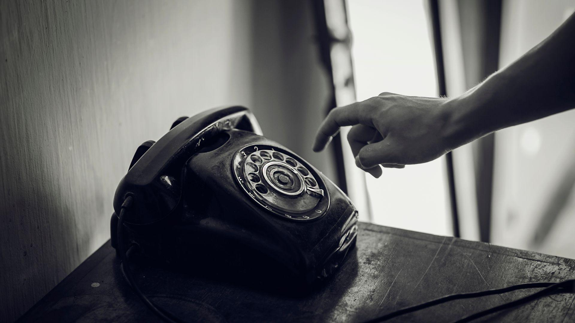 A hand reaching for an old rotary telephone in black and white